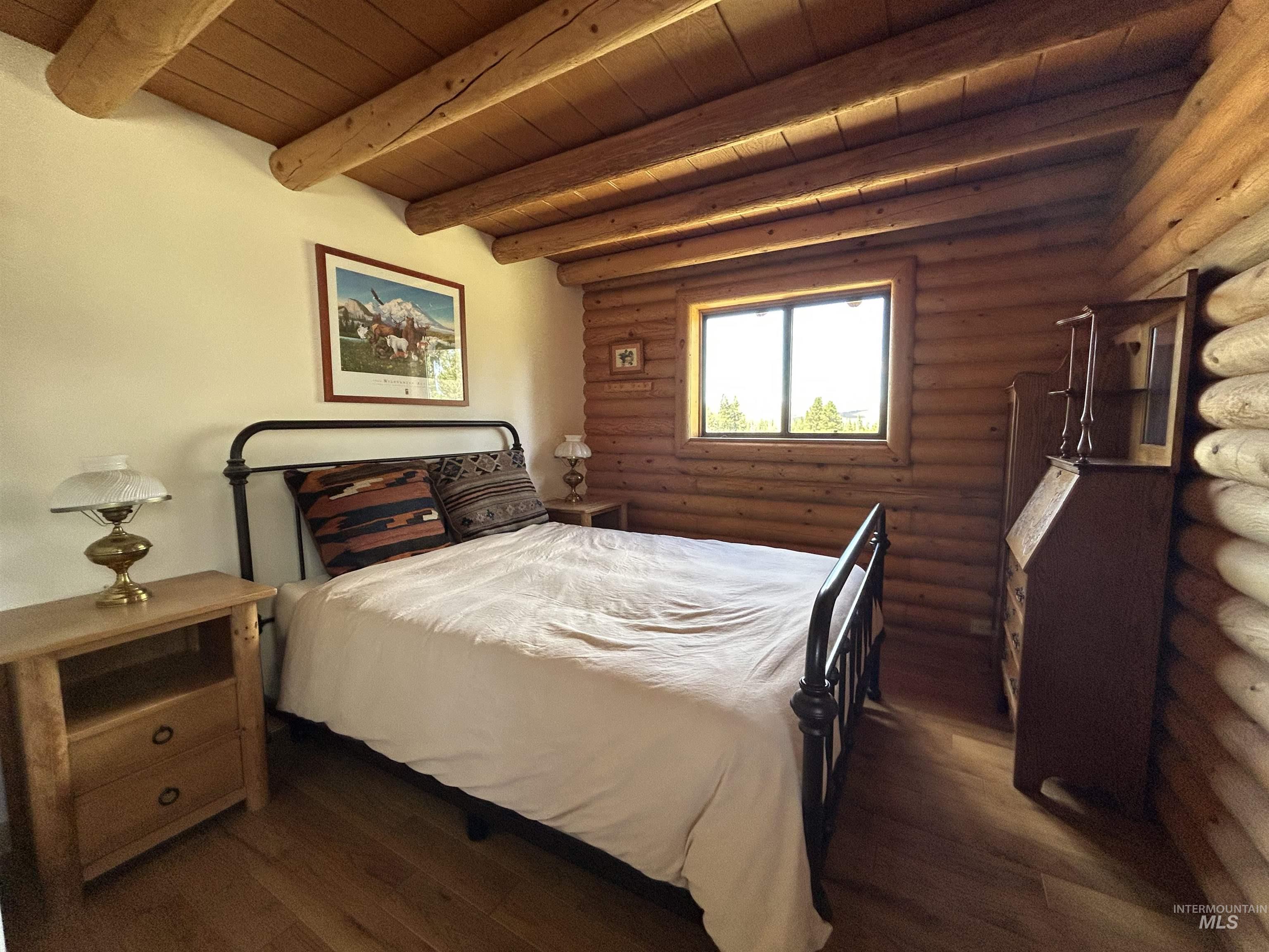 35 Sawtooth Way Stanley, ID 83278 - Photo 20 of 36 Bedroom featuring exposed log walls, wood-finish flooring, a window with wood trim, and a log-beamed ceiling
