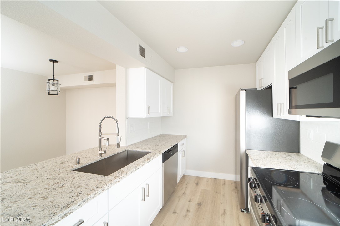 8101 West Flamingo Road, Unit 1057 Las Vegas, NV 89147 - Photo 2 of 38 Kitchen with stainless steel appliances, light wood-style floors, hanging light fixtures, light stone counters, and white cabinetry