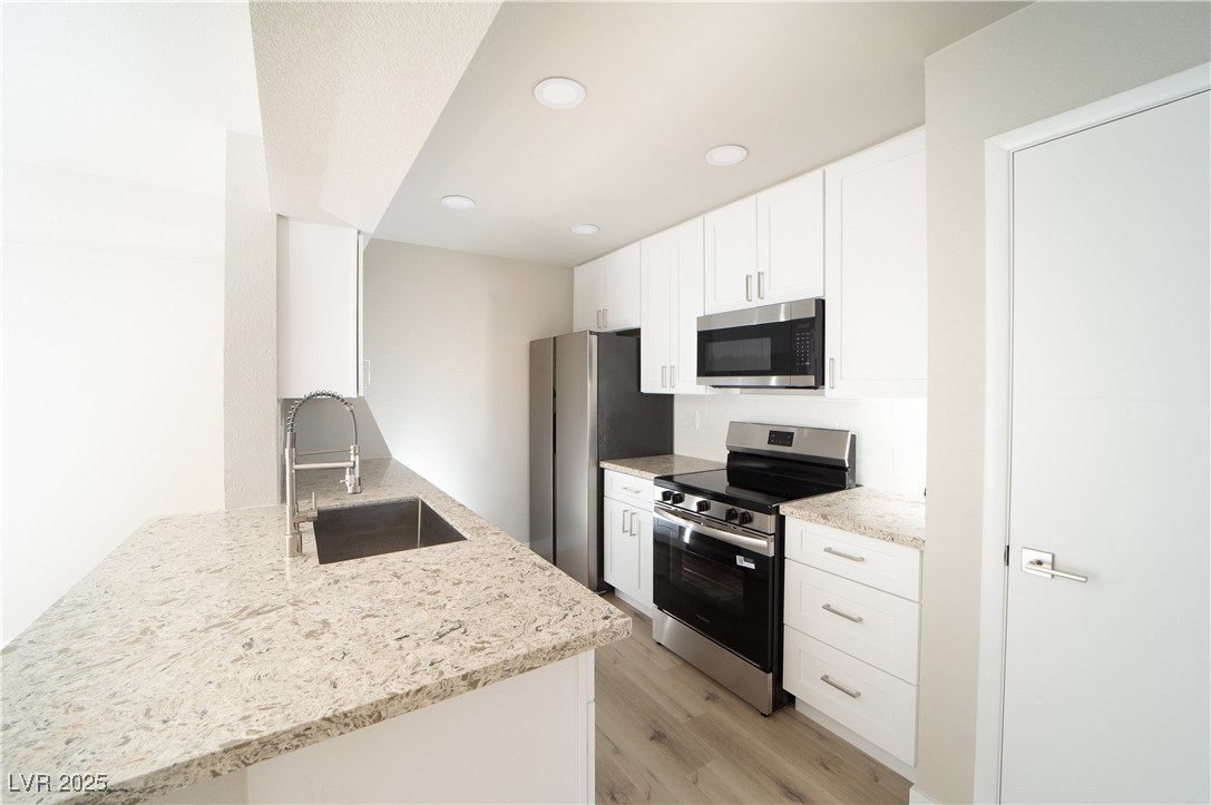 8101 West Flamingo Road, Unit 1057 Las Vegas, NV 89147 - Photo 3 of 38 Kitchen with appliances with stainless steel finishes, white cabinets, light stone counters, light wood finished floors, and recessed lighting