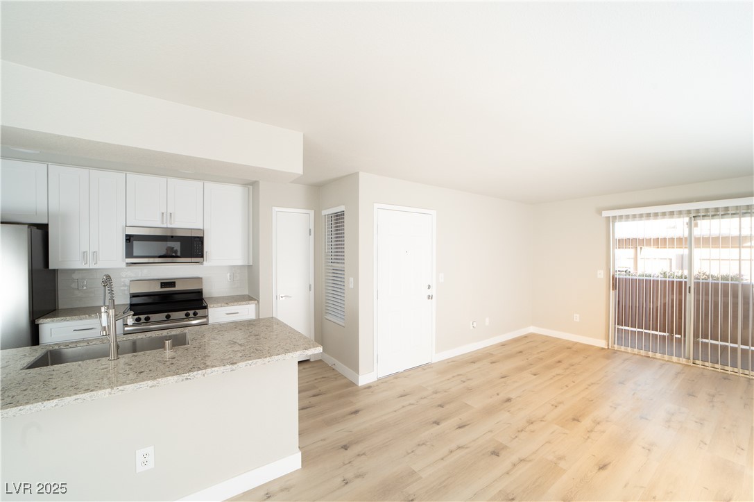 8101 West Flamingo Road, Unit 1057 Las Vegas, NV 89147 - Photo 4 of 38 Kitchen featuring white cabinets, light stone counters, stainless steel appliances, light wood-style flooring, and tasteful backsplash