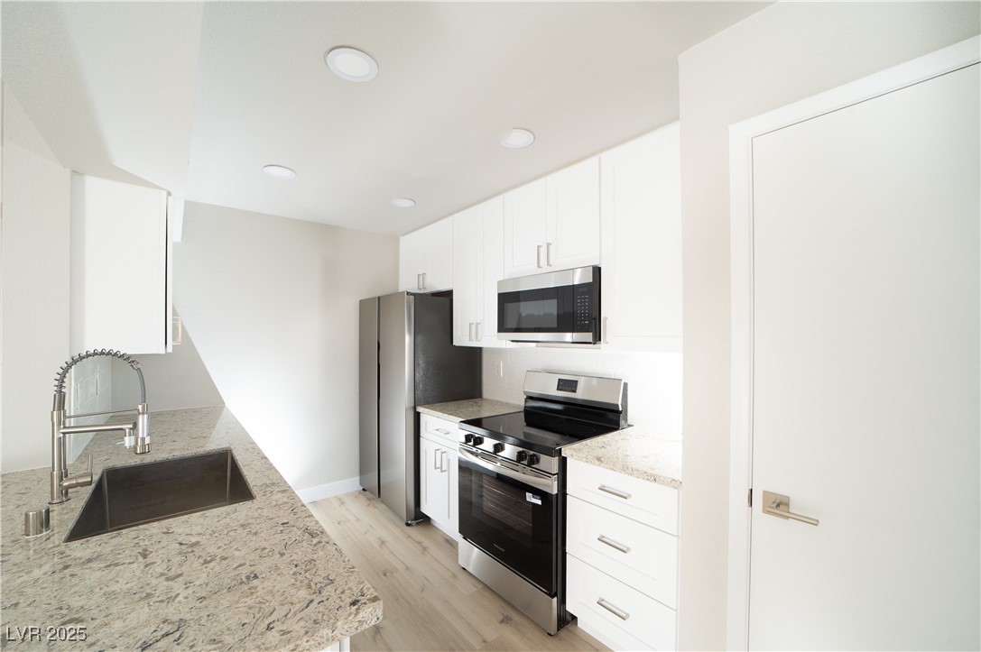 8101 West Flamingo Road, Unit 1057 Las Vegas, NV 89147 - Photo 5 of 38 Kitchen with stainless steel appliances, light stone countertops, white cabinets, light wood-style floors, and recessed lighting