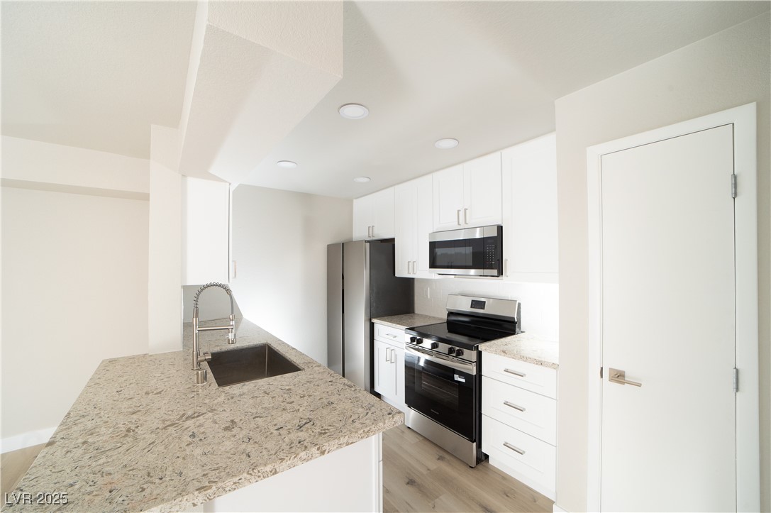 8101 West Flamingo Road, Unit 1057 Las Vegas, NV 89147 - Photo 6 of 38 Kitchen featuring stainless steel appliances, white cabinets, light stone counters, light wood finished floors, and a peninsula