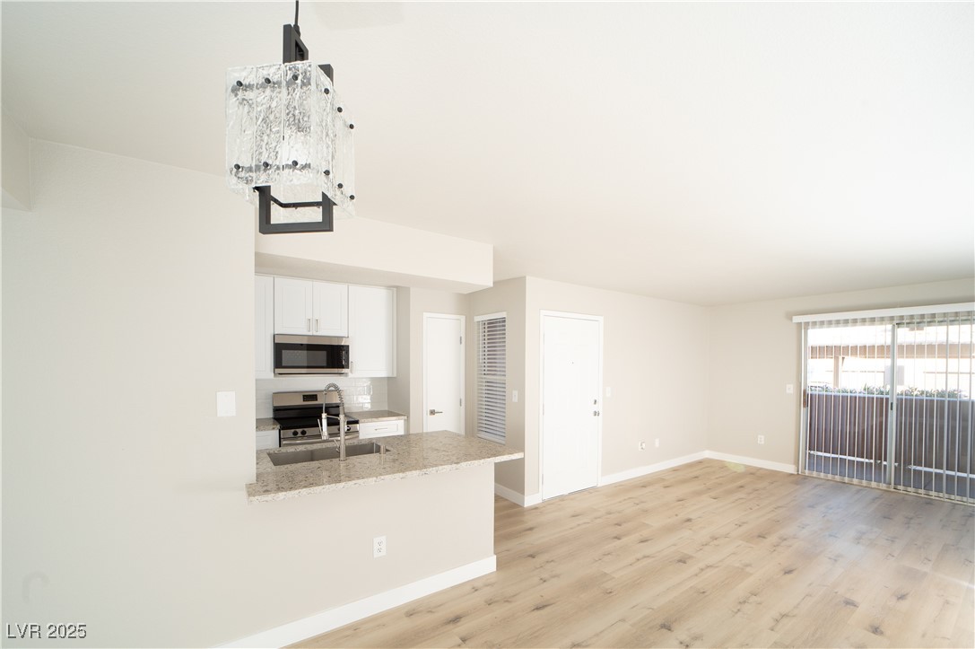 8101 West Flamingo Road, Unit 1057 Las Vegas, NV 89147 - Photo 7 of 38 Kitchen with tasteful backsplash, white cabinetry, stainless steel appliances, light stone countertops, and light wood finished floors