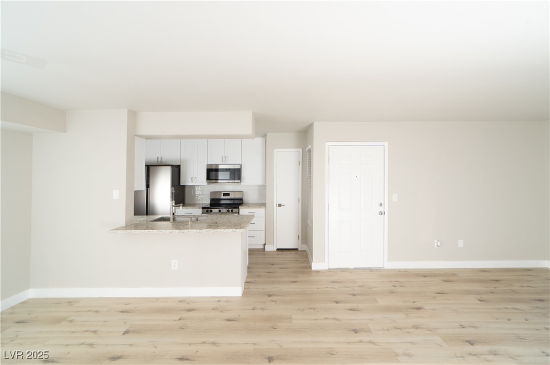 8101 West Flamingo Road, Unit 1057 Las Vegas, NV 89147 - Photo 8 of 38 Kitchen featuring light wood-style floors, stainless steel appliances, white cabinetry, light stone countertops, and a peninsula