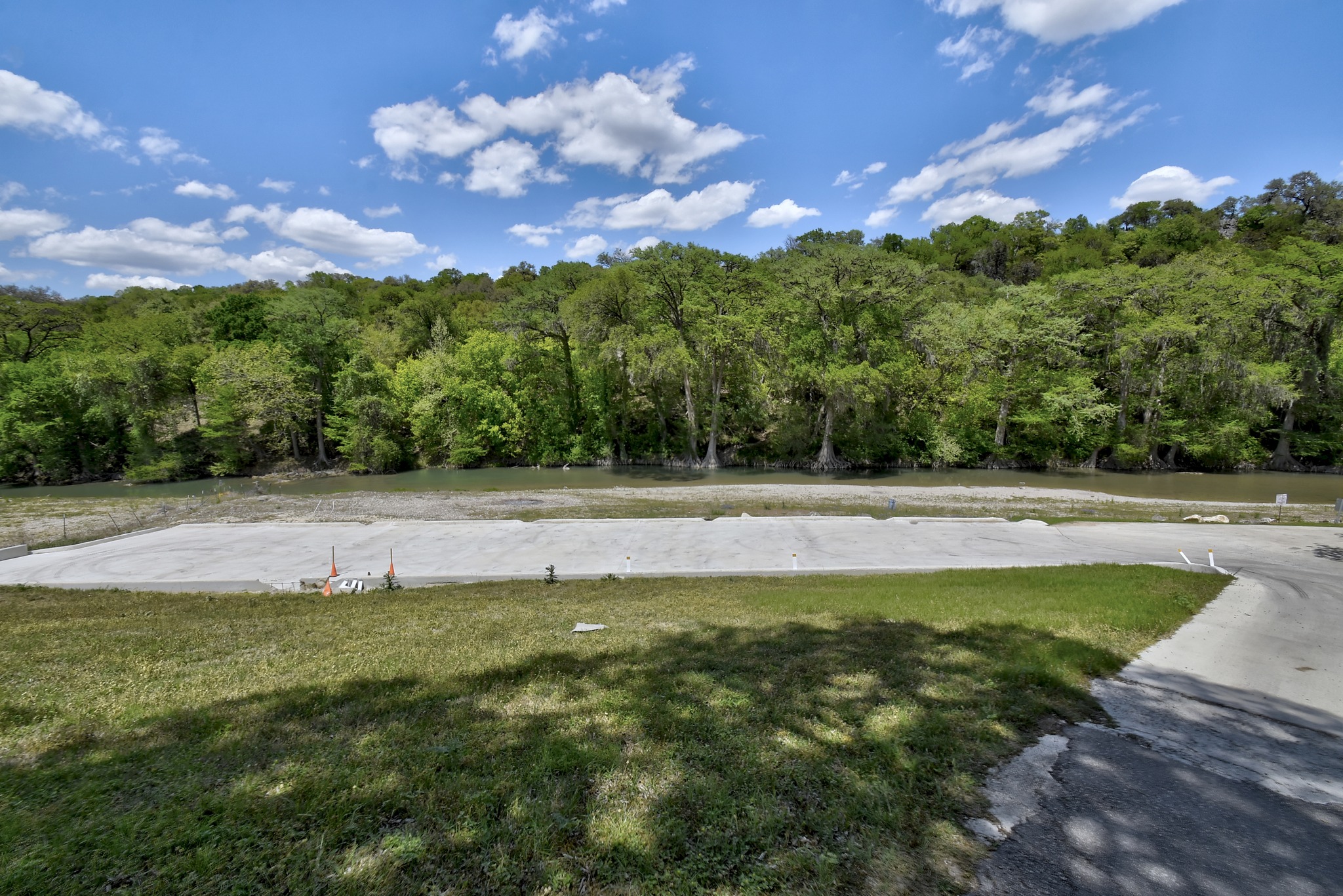 1170 Misty Lane Spring Branch, TX 78070 - Photo 10 of 24 A tranquil river flows past a verdant forest, with a spacious paved area leading to the water.