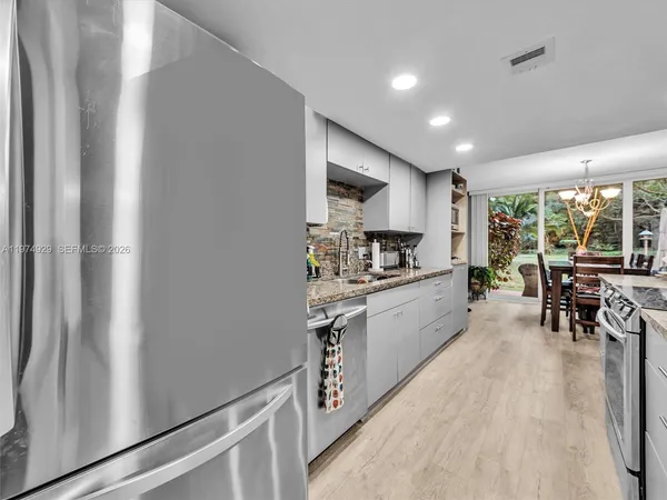 a kitchen with stainless steel appliances granite countertop a refrigerator a stove a dining table and chairs with wooden floor