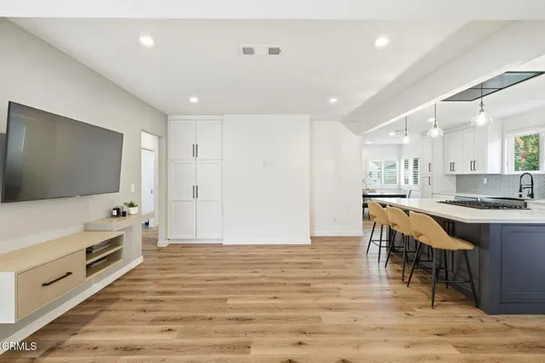 a large white kitchen with stainless steel appliances granite countertop a stove a sink a refrigerator and a dining table with wooden floor