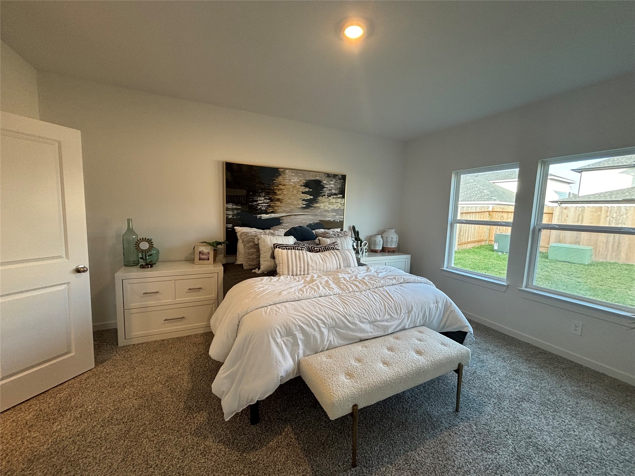 4315 Windsor Forest Fulshear, TX 77494 - Photo 13 of 50 This Spacious Primary bedroom on main floor features a plush carpet, a comfortable bed with a cushioned bench at the foot, and large windows providing ample natural light and a view of the backyard. Neutral decor creates a serene atmosphere.