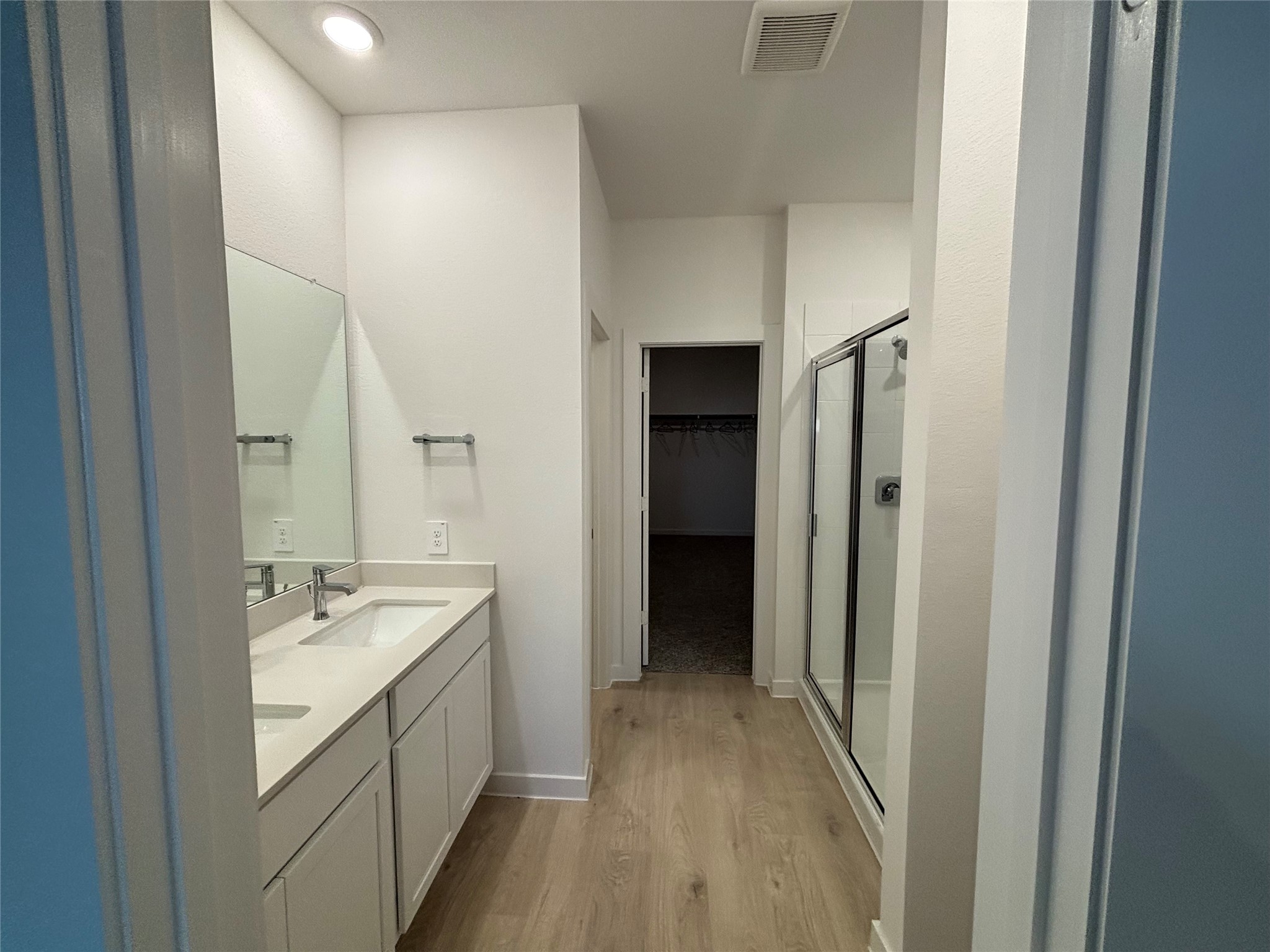 4315 Windsor Forest Fulshear, TX 77494 - Photo 15 of 50 This modern bathroom features a double vanity with ample storage, a spacious glass-enclosed shower, and a walk-in closet. The light wood flooring and recessed lighting create a bright and inviting atmosphere.