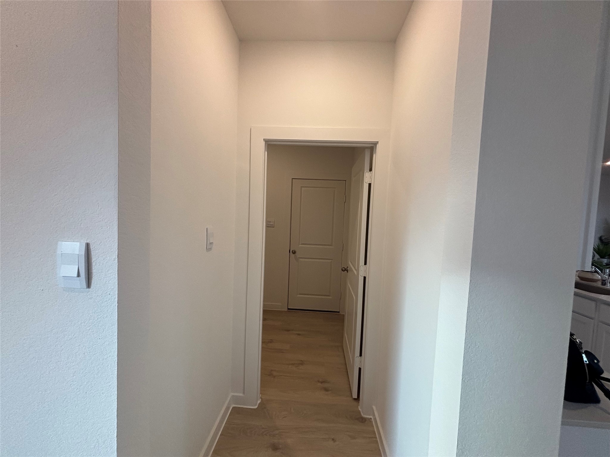 4315 Windsor Forest Fulshear, TX 77494 - Photo 21 of 50 This photo shows a hallway with light-colored walls and wood flooring, leading to a closed door. The space appears clean and well-maintained, with a light switch visible on the left wall.