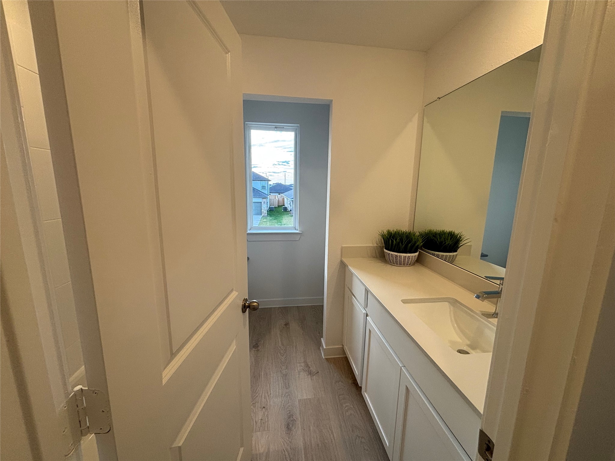 4315 Windsor Forest Fulshear, TX 77494 - Photo 22 of 50 This is a one of the secondary bathroom on the left side of gameroom as you climb the stairs featuring a single vanity with a modern faucet, a large mirror, and two decorative plants. It has wood-like flooring and a window providing natural light.
