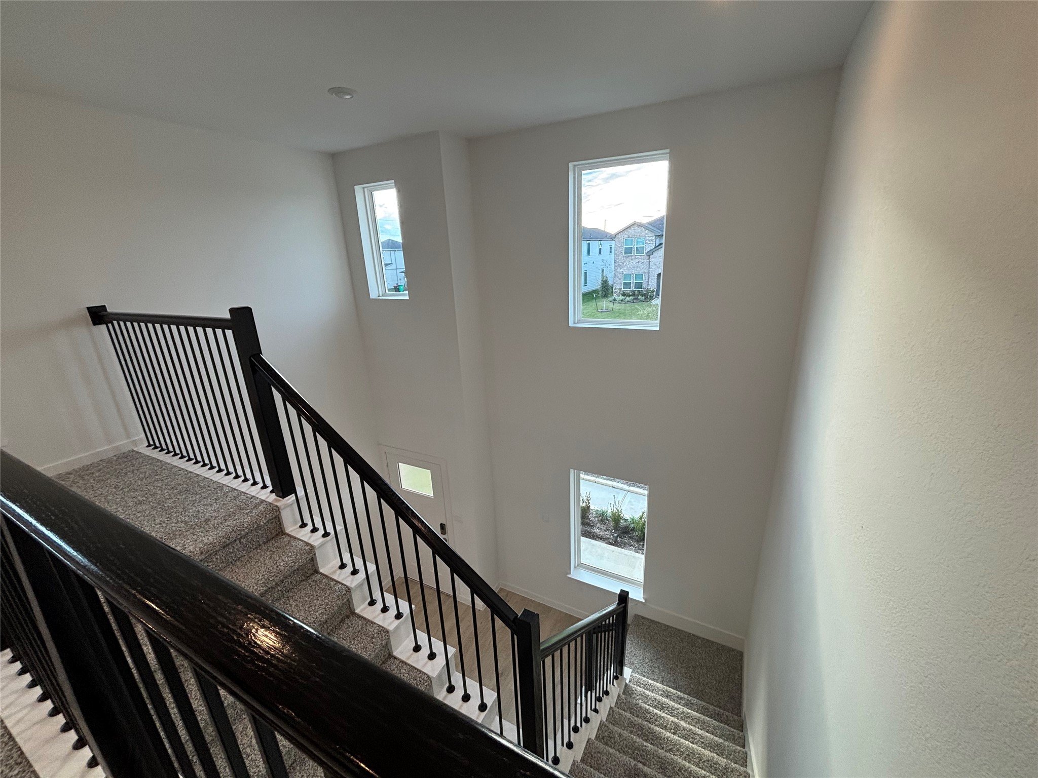 4315 Windsor Forest Fulshear, TX 77494 - Photo 24 of 50 This photo shows a modern, carpeted staircase with sleek black railings. The stairwell is well-lit by three tall windows, offering a view of the surrounding neighborhood. The space is bright and open, providing a welcoming transition between floors.