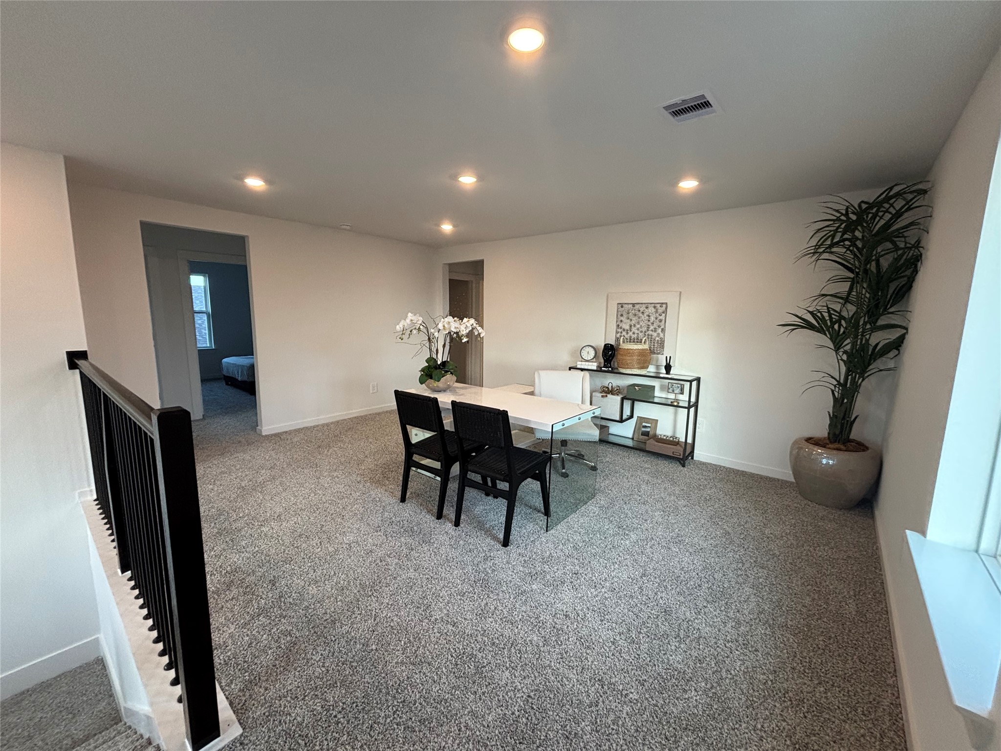 4315 Windsor Forest Fulshear, TX 77494 - Photo 25 of 50 This spacious game room on 2nd floor features plush carpeting, recessed lighting, and a modern open layout. It includes a versatile area with a desk and seating, ideal for a home office or study. A large potted plant adds a touch of greenery, while nearby doorways lead to adjacent rooms.