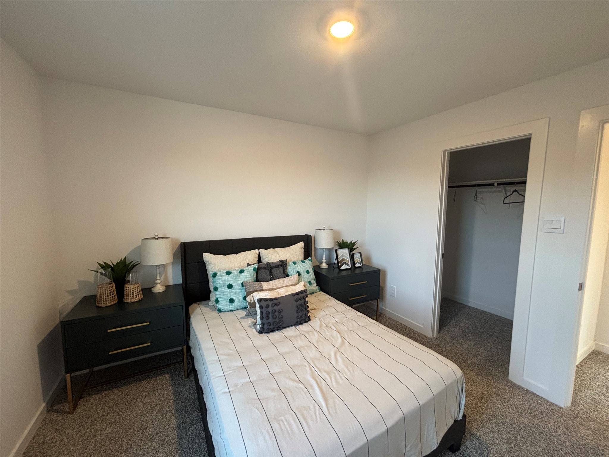 4315 Windsor Forest Fulshear, TX 77494 - Photo 30 of 50 This bedroom features a cozy, modern design with a neatly made bed, two stylish nightstands with lamps, and an open closet. The room is carpeted and has a warm, inviting atmosphere.