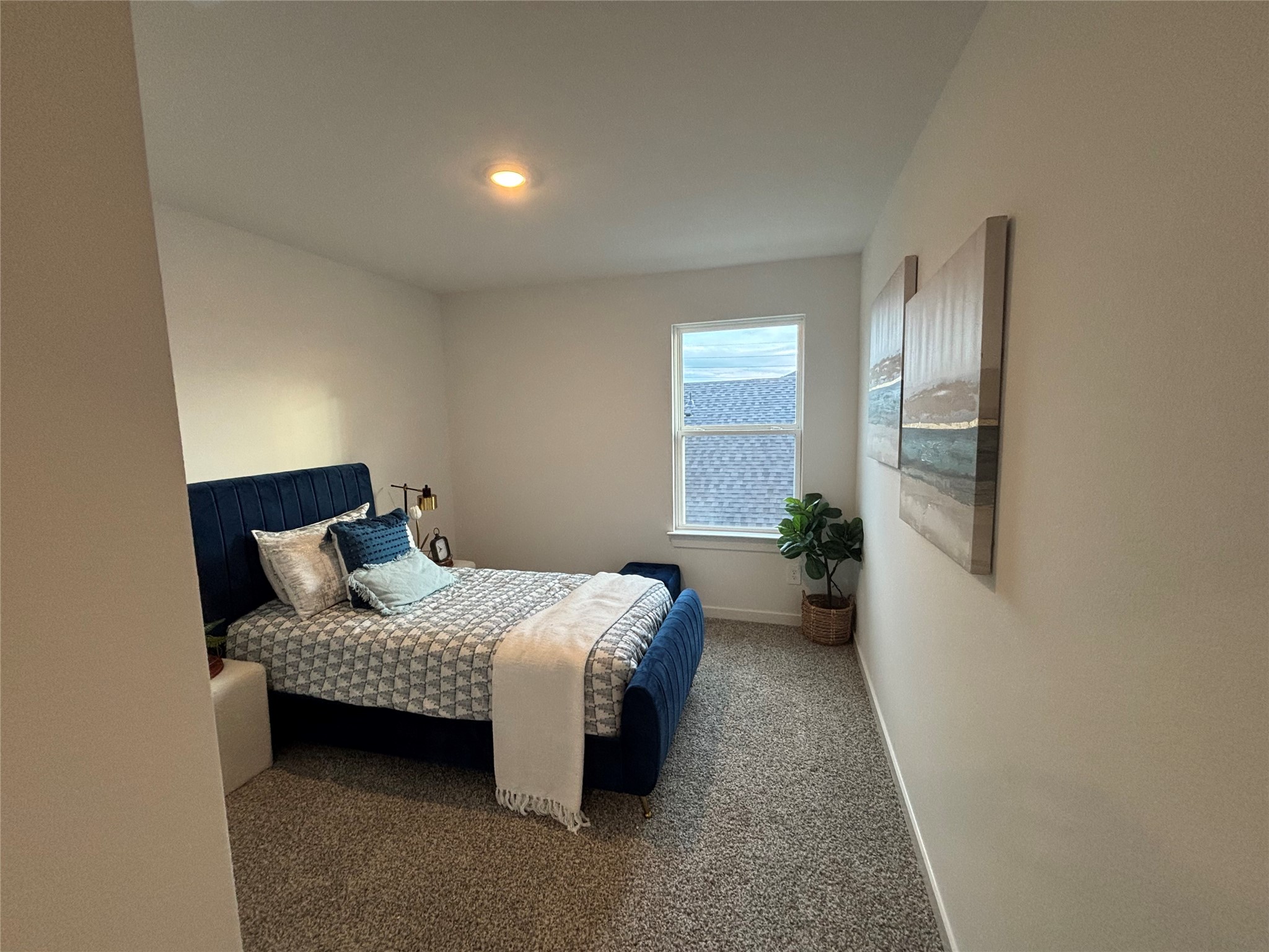4315 Windsor Forest Fulshear, TX 77494 - Photo 32 of 50 A cozy bedroom with neutral walls and carpet, featuring a comfortable bed with blue accents, a window providing natural light, and tasteful decor including wall art and a potted plant.