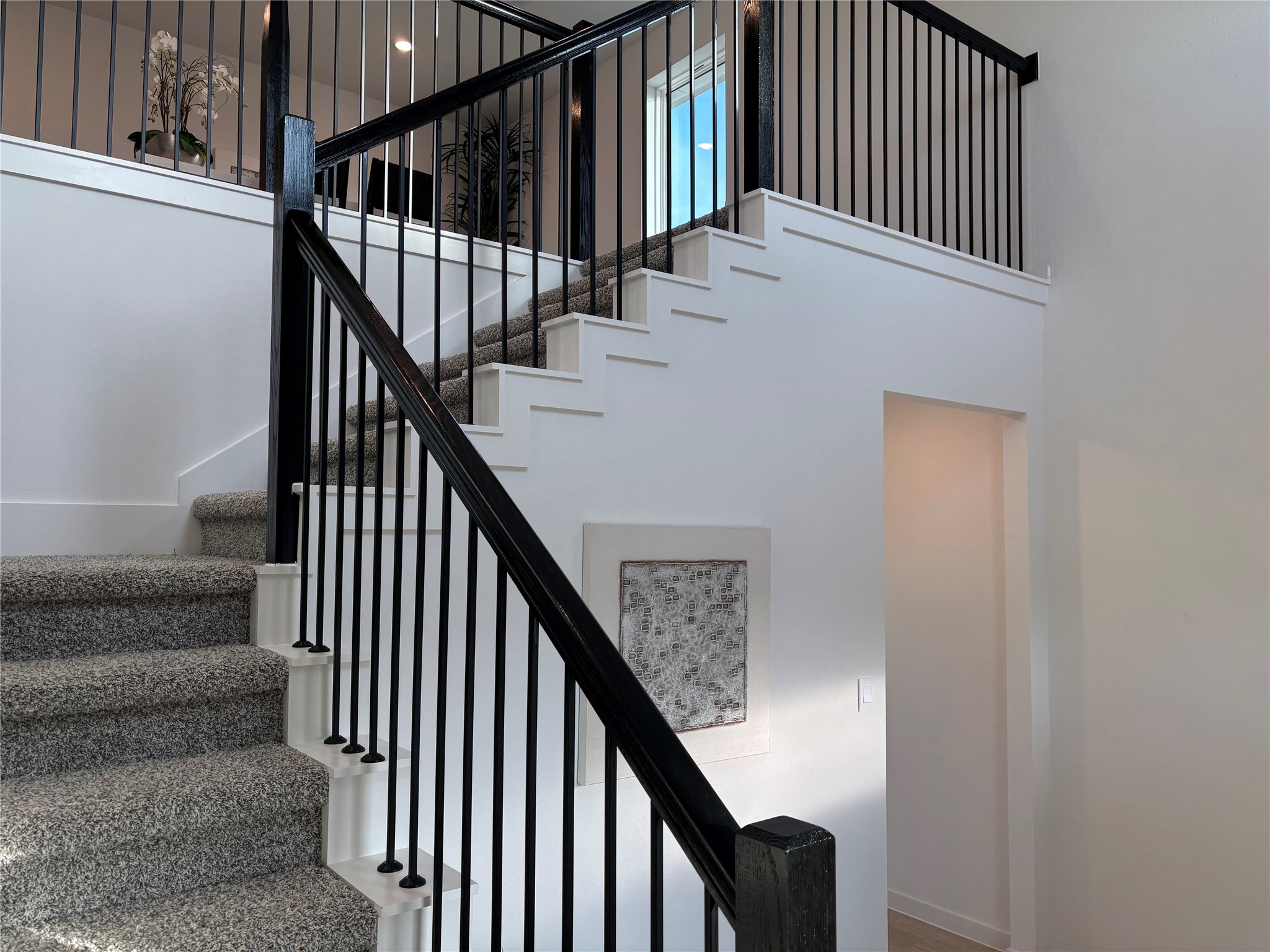 4315 Windsor Forest Fulshear, TX 77494 - Photo 5 of 50 Modern staircase with dark railings and light carpet, leading to an open upper landing. The design is clean and contemporary, with bright walls and a small artwork accent.