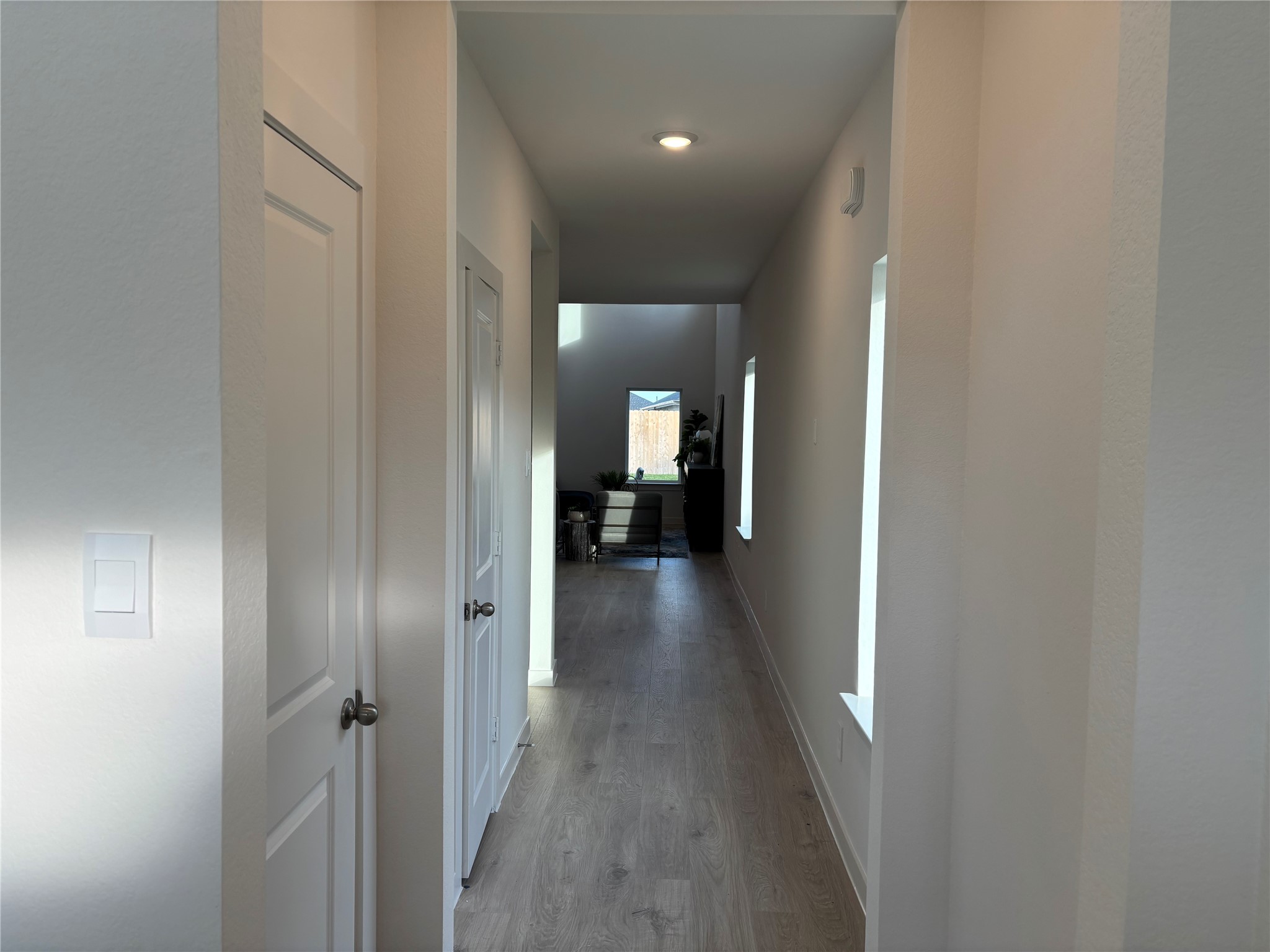 4315 Windsor Forest Fulshear, TX 77494 - Photo 7 of 50 This photo shows a bright, long hallway with light wood flooring and white walls. It leads to a room with a window at the end, allowing natural light to fill the space.