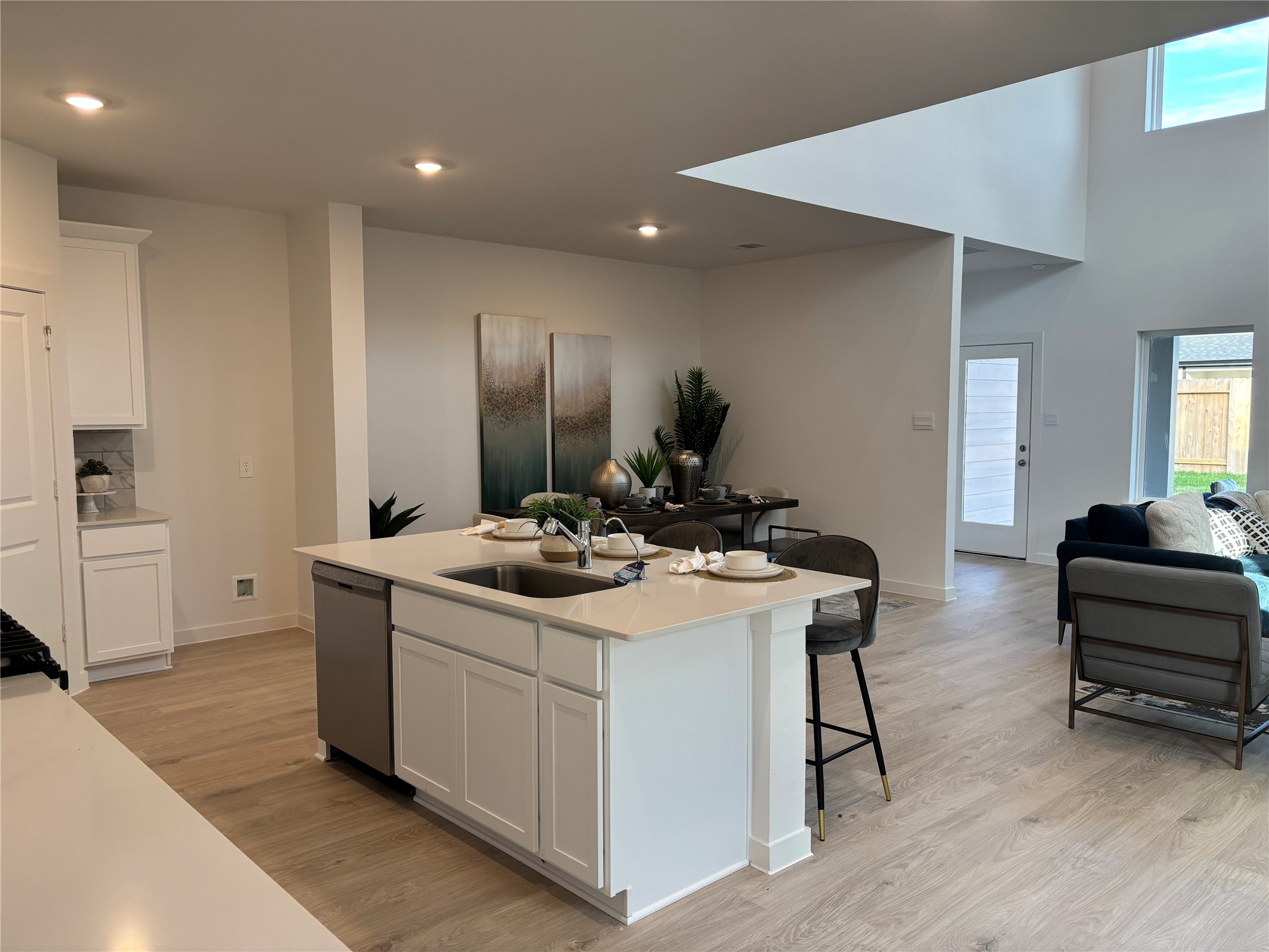 4315 Windsor Forest Fulshear, TX 77494 - Photo 9 of 50 This photo showcases a modern open-concept living space with high ceilings. It features a sleek kitchen island with bar seating, light wood flooring, and a bright living area with large windows that offer plenty of natural light.