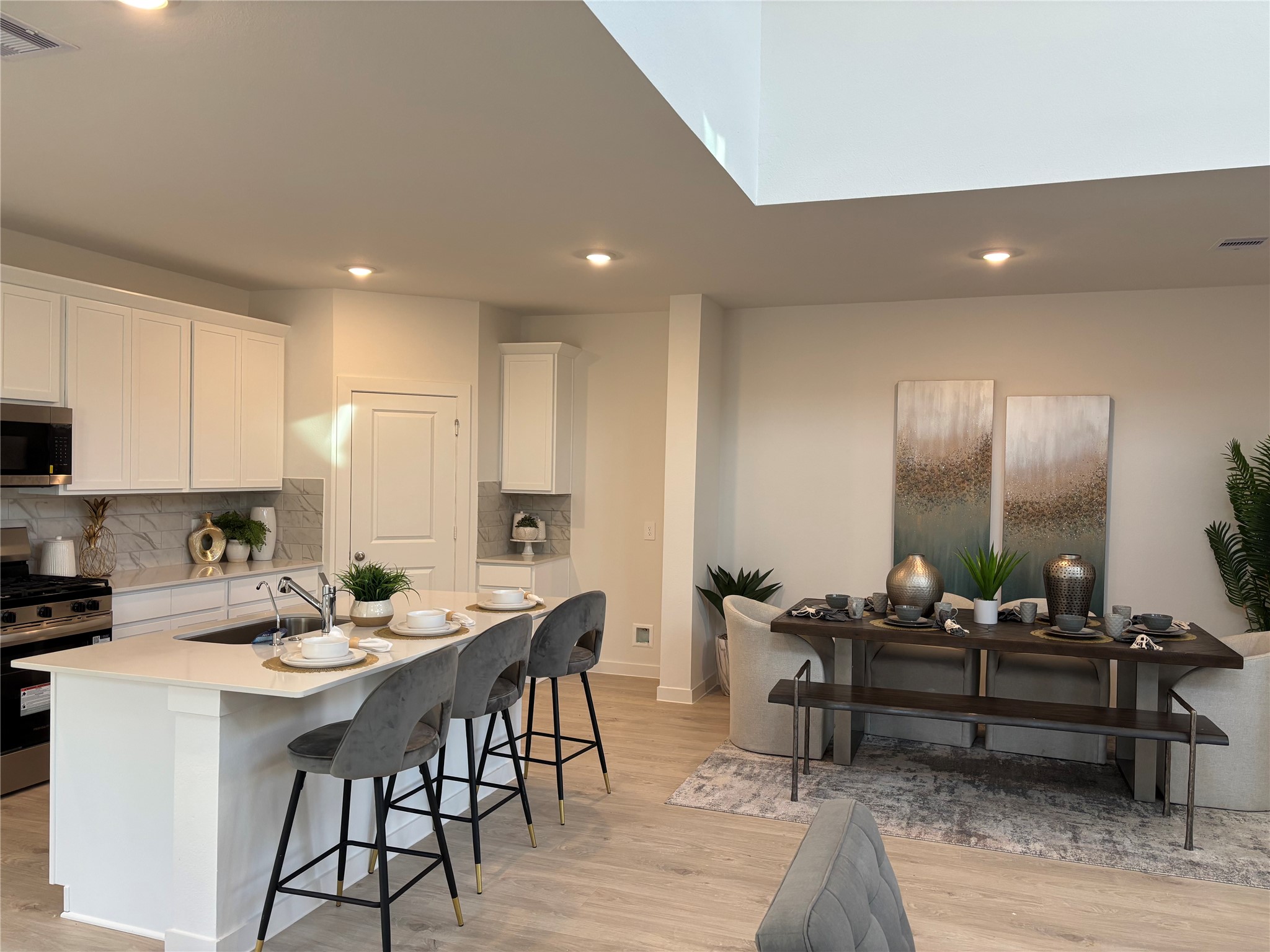 4315 Windsor Forest Fulshear, TX 77494 - Photo 10 of 50 This photo showcases a modern open-concept kitchen and dining area. The kitchen features white cabinetry, stainless steel appliances, and an island with seating. The dining area includes a stylish table set against neutral decor and artwork, creating a warm and inviting space.