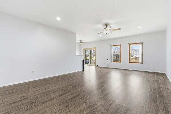 an empty room with wooden floor ceiling fan and windows