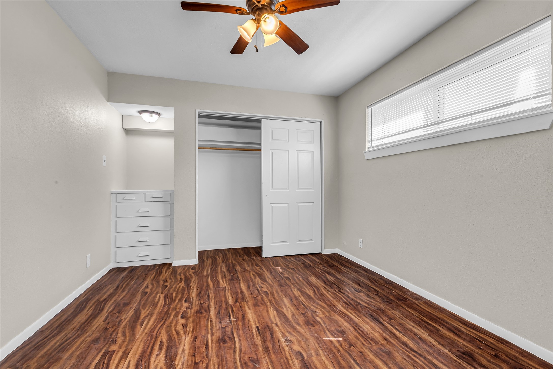 4706 Yellowstone Boulevard, Unit 5 Houston, TX 77021 - Photo 11 of 14 This room features warm wood laminate flooring, neutral walls, and ample natural light from a high-set window. It includes a ceiling fan, built-in drawers, and a closet with sliding doors, offering both comfort and storage.