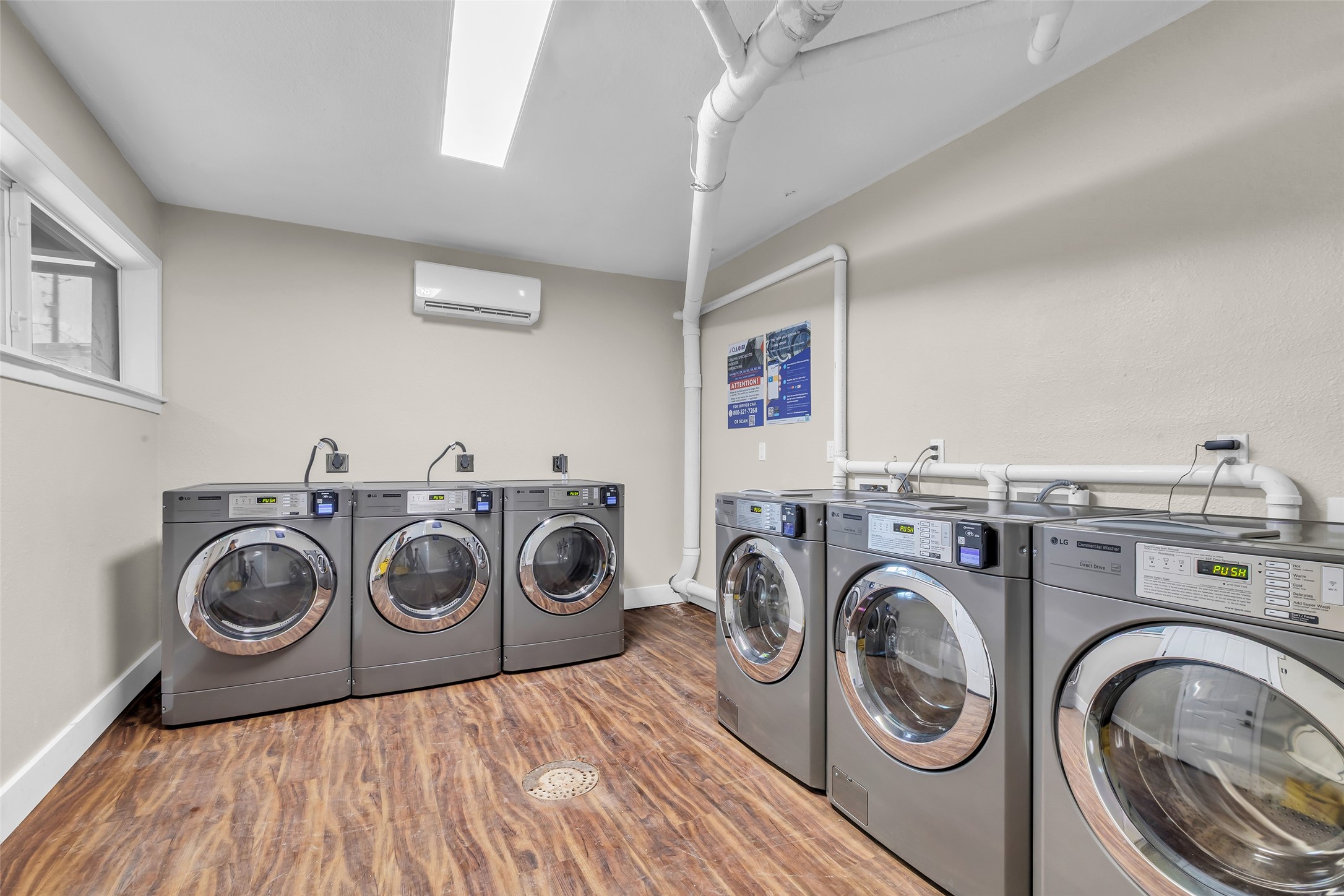 4706 Yellowstone Boulevard, Unit 5 Houston, TX 77021 - Photo 13 of 14 This photo shows a modern laundry room with six stainless steel front-loading washers. The room features wood-style flooring, neutral walls, and overhead lighting, creating a clean and functional space.