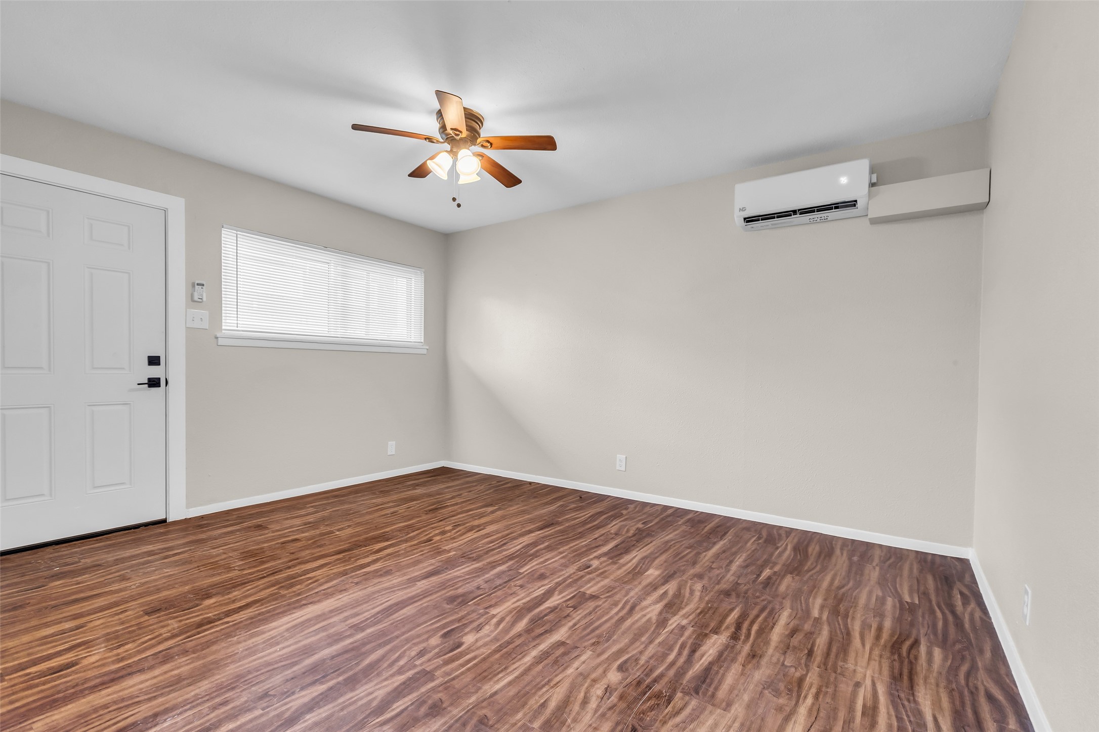 4706 Yellowstone Boulevard, Unit 5 Houston, TX 77021 - Photo 8 of 14 This room features wood-look flooring, neutral walls, a ceiling fan with lights, and a wall-mounted air conditioning unit. It includes a window and an entrance door, creating a bright and functional space.