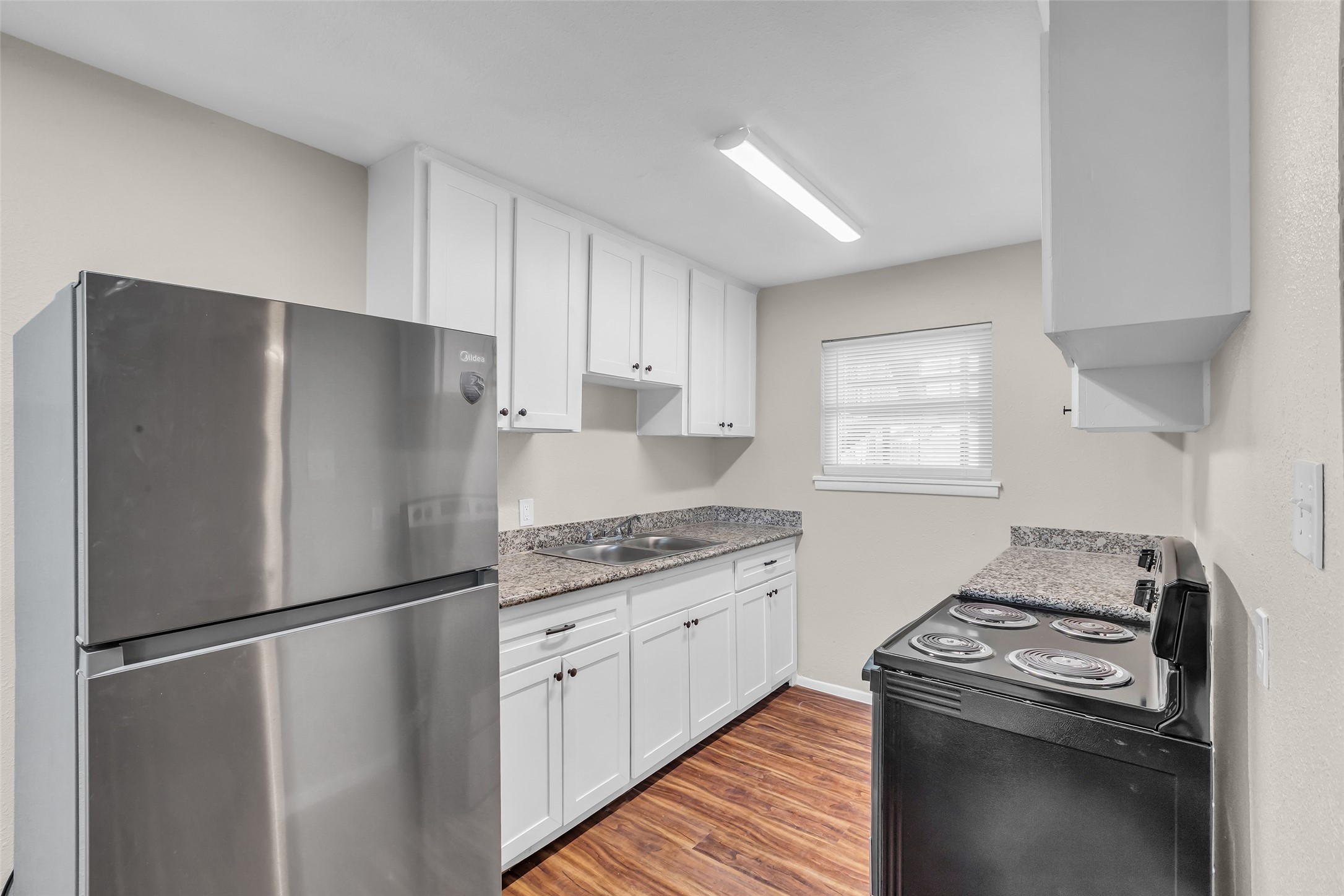 4706 Yellowstone Boulevard, Unit 5 Houston, TX 77021 - Photo 10 of 14 This kitchen features modern stainless steel appliances, sleek white cabinetry, and granite countertops. It has a compact layout with wood-style flooring and a bright window for natural light.