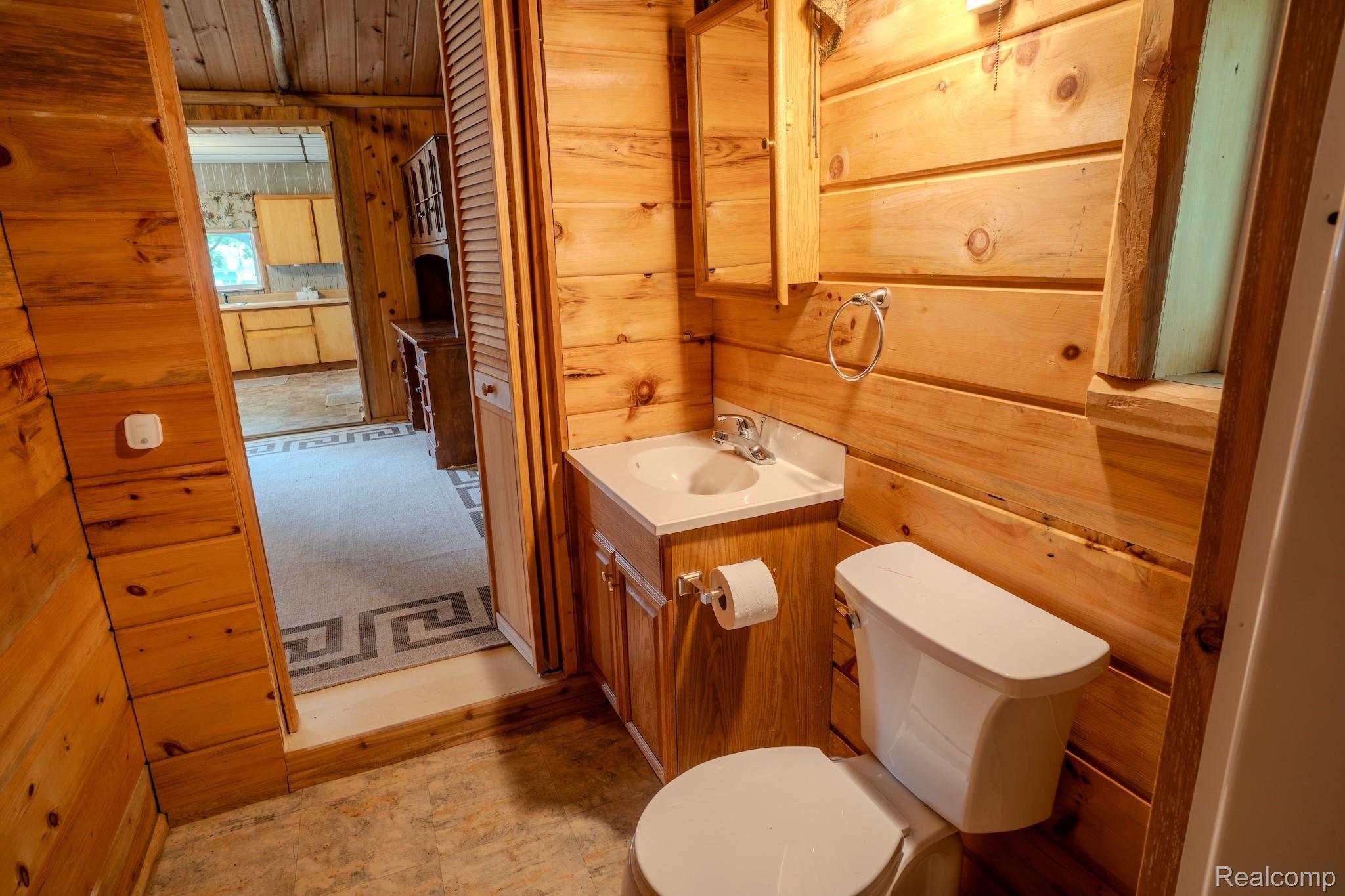 4350 Shrew Road Lincoln, MI 48742 - Photo 21 of 32 Bathroom featuring wood-paneled walls, a white vanity with a ceramic sink, a wall-mounted mirror cabinet, and a white toilet