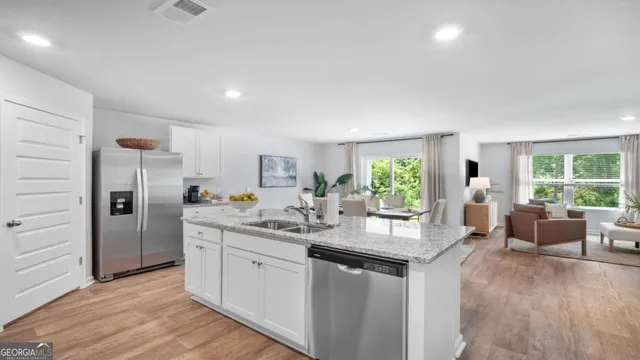 a kitchen with stainless steel appliances granite countertop a refrigerator a sink dishwasher a stove and white countertops with wooden floor