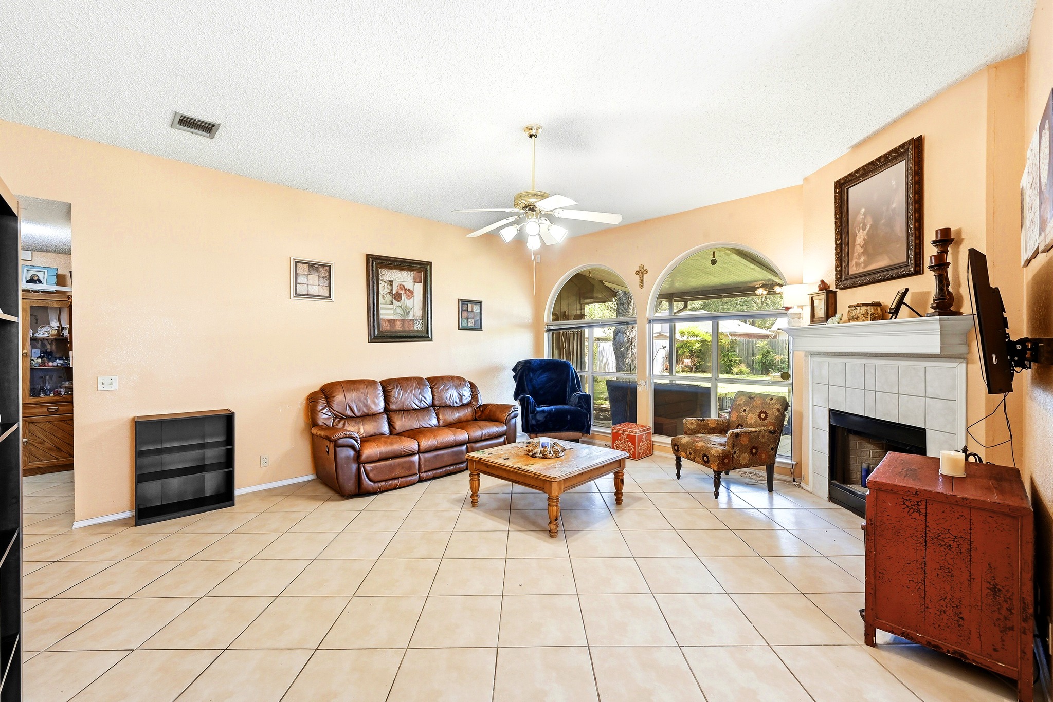 6412 Colton-Bluff Springs Road Austin, TX 78744 - Photo 4 of 27 A tiled living room with a cozy fireplace and arched windows overlooking the outdoor area.