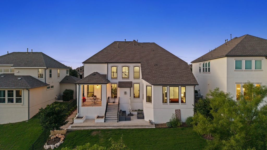 1221 Siena Sunset Road Leander, TX 78641 - Photo 38 of 39 Rear exterior featuring a covered patio, multiple large windows, a terraced yard with a stone-edged garden bed, and a stucco finish