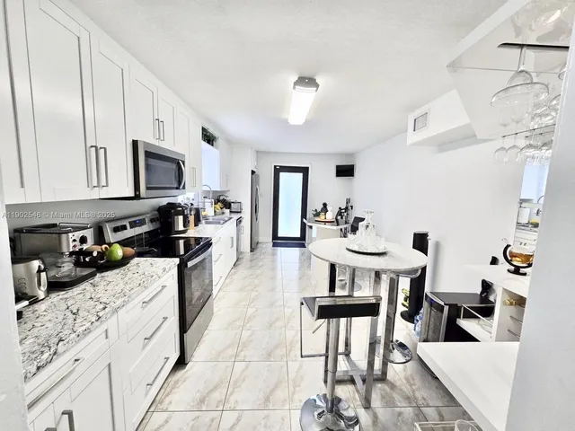 a kitchen with stainless steel appliances kitchen island granite countertop a stove a sink a dining table and chairs with white cabinets