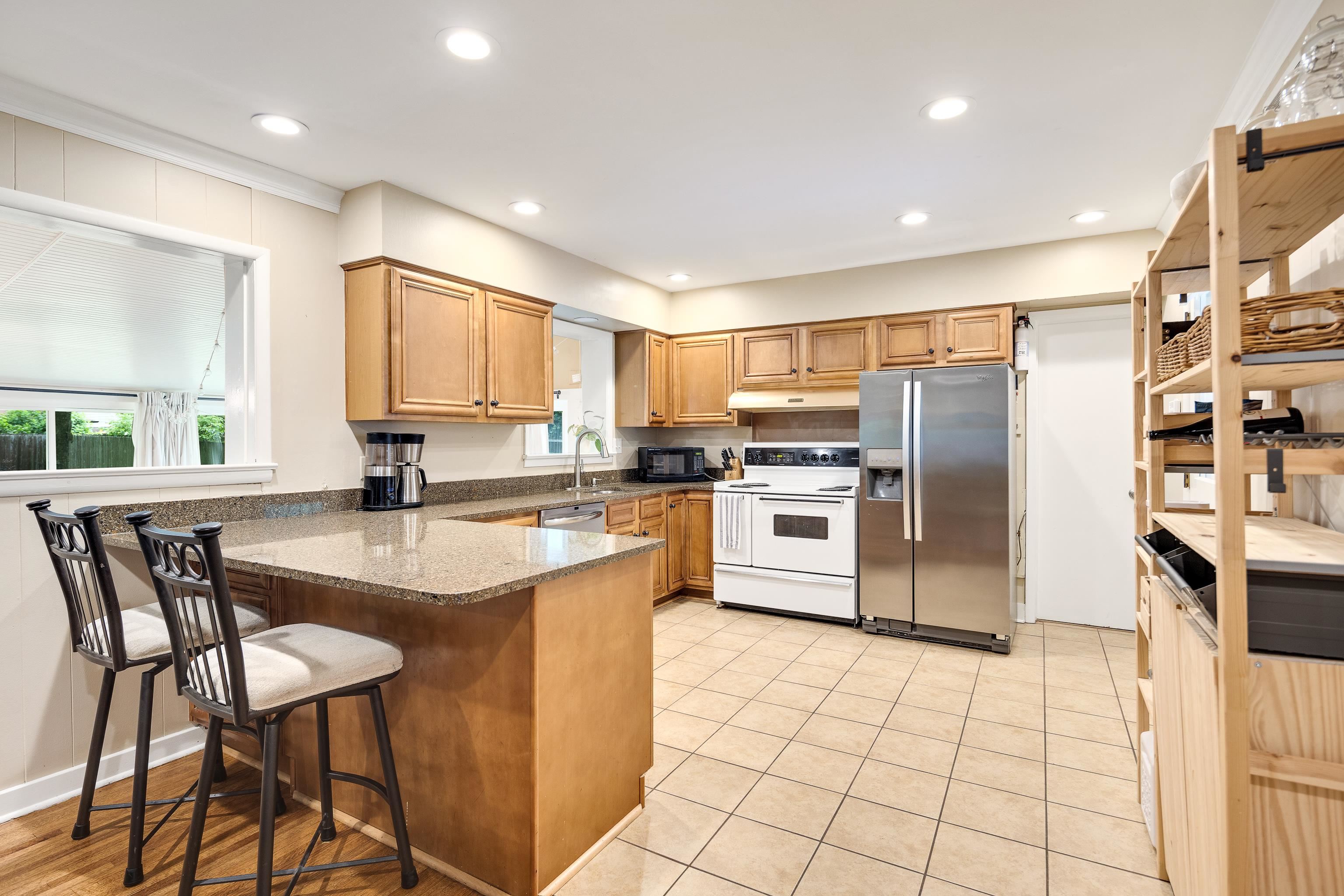 4152 Barfield Road Memphis, TN 38117 - Photo 18 of 37 Kitchen featuring stainless steel appliances, brown cabinetry, a peninsula, dark stone countertops, and a kitchen bar