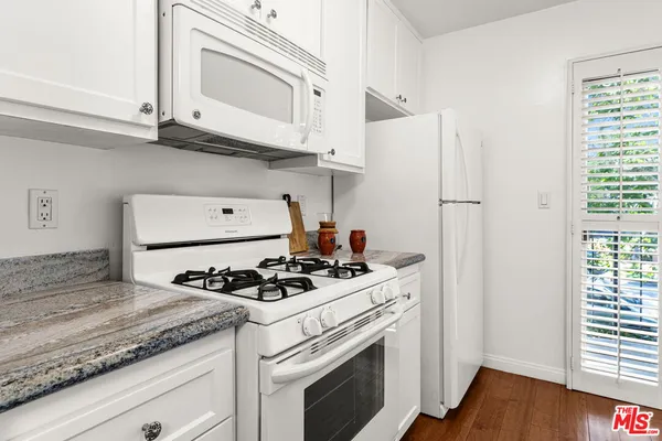 a kitchen with granite countertop white cabinets white appliances and a wide window