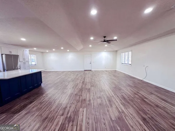 a view of an empty room with wooden floor and a kitchen