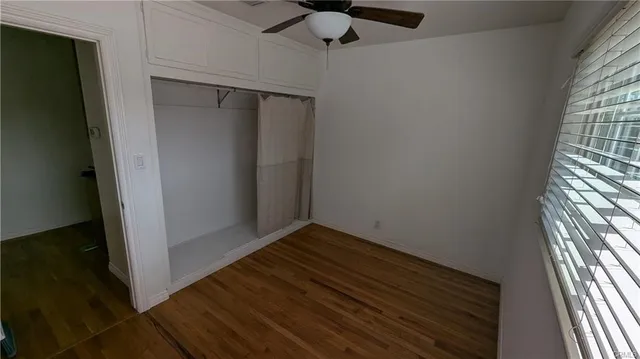 an empty room with wooden floor fan and windows