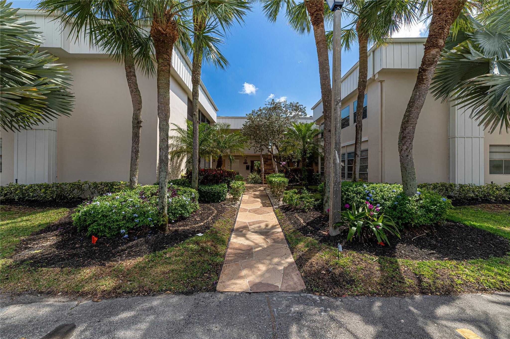 103 Capri B, Unit 103 Delray Beach, FL 33484 - Photo 16 of 24 a view of a pathway besides a house with a yard and potted plants