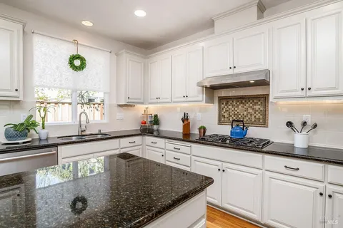 a kitchen with stainless steel appliances granite countertop a sink a stove white cabinets and a window