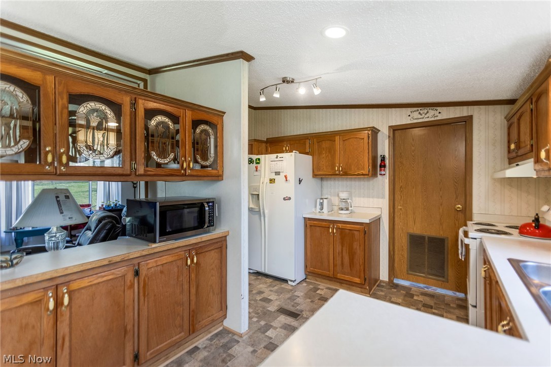 4502 Clover Road Cumberland, OH 43732 - Photo 11 of 38 Kitchen featuring wood finish cabinetry, glass insert cabinets, light countertops, white appliances, and crown molding
