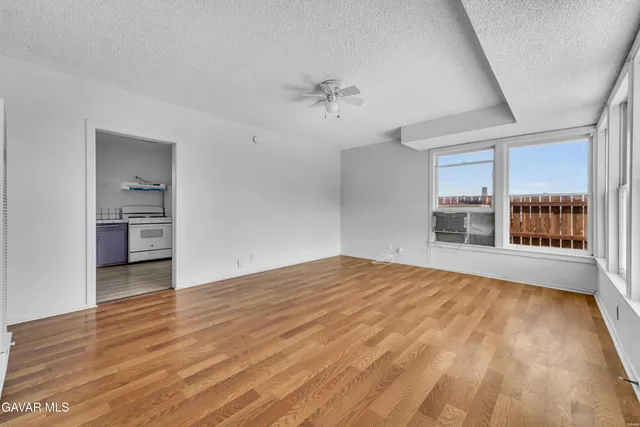 a view of empty room with wooden floor and kitchen view