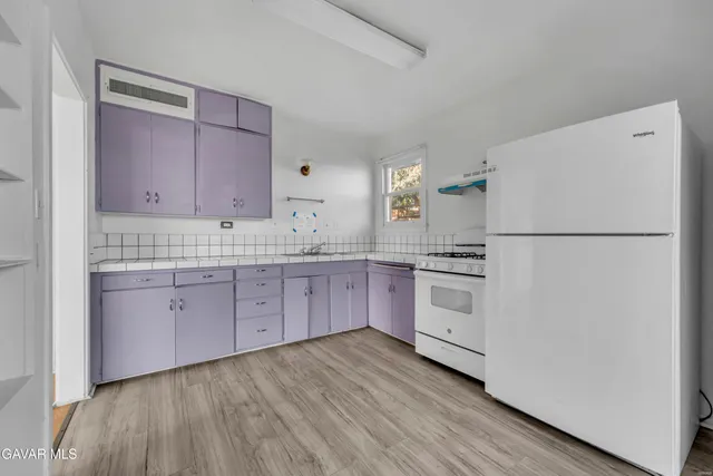 a kitchen with granite countertop a white refrigerator oven a sink with cabinets and wooden floor