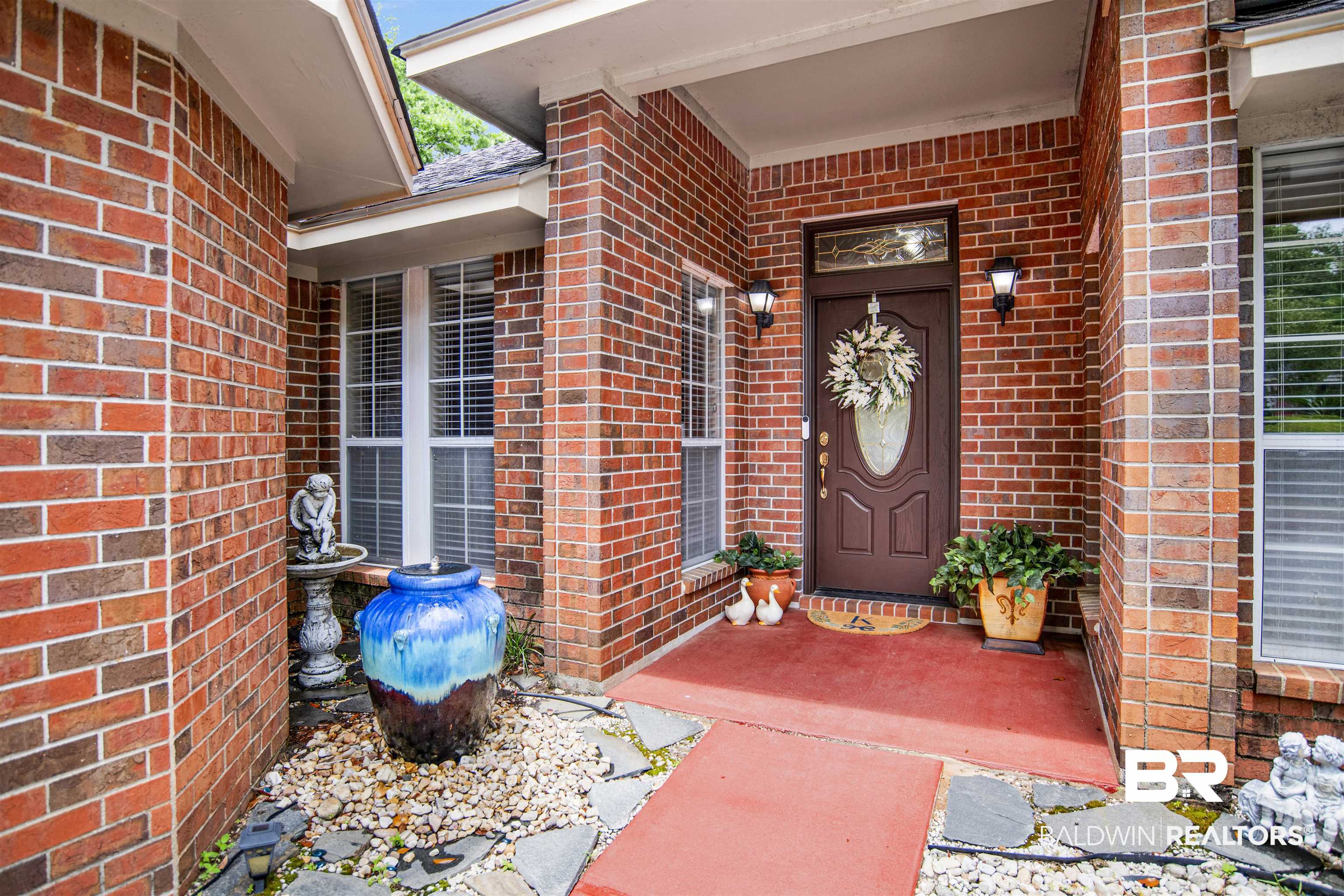 107 Virginia Circle Daphne, AL 36526 - Photo 5 of 47 Brick exterior featuring a covered entry, dark wood front door with decorative glass inlay, and flanking windows with white blinds