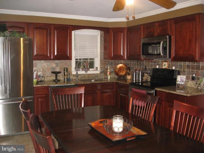 5345 Huntingtown Road Huntingtown, MD 20639 - Photo 7 of 12 a kitchen with granite countertop a stove a sink dishwasher a dining table and chairs with wooden floor