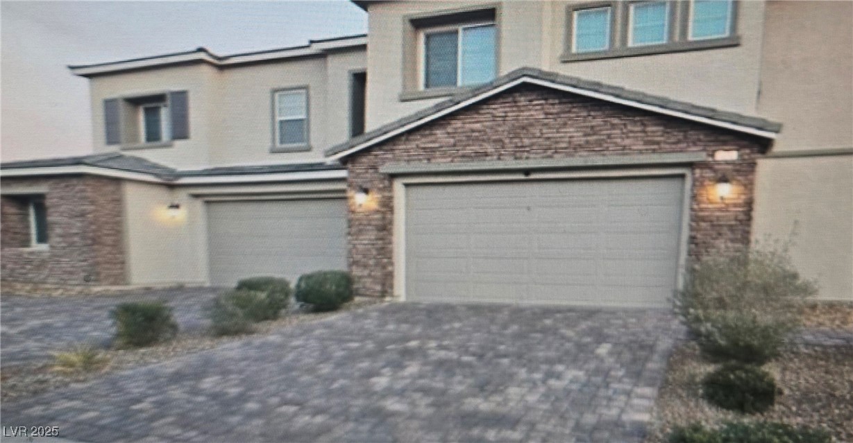 View of front facade featuring decorative driveway, brick siding, and a garage