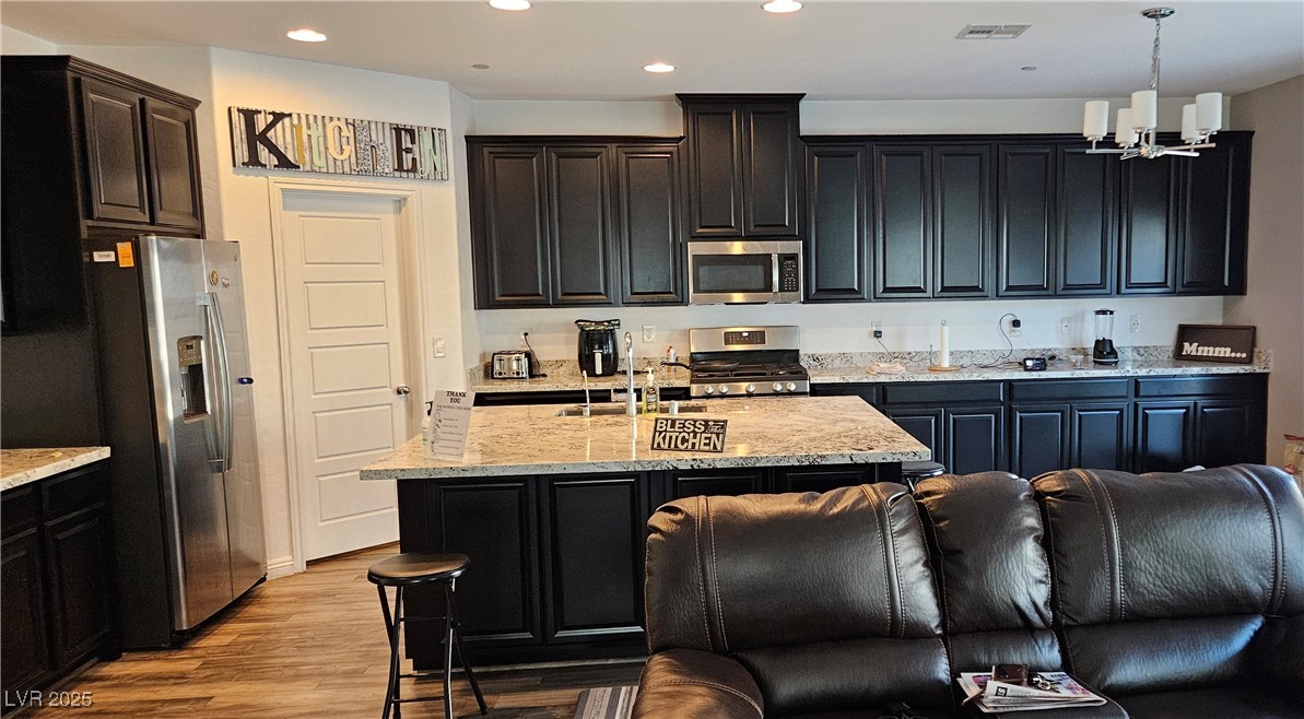 7050 Fossil Rim Street North Las Vegas, NV 89084 - Photo 4 of 19 Kitchen featuring dark cabinetry, stainless steel appliances, light stone countertops, recessed lighting, and a center island with sink