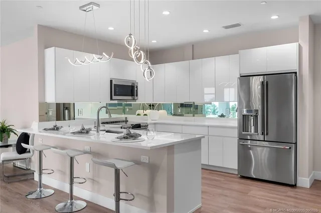 a kitchen with stainless steel appliances granite countertop a refrigerator a sink dishwasher a stove and white cabinets with wooden floor