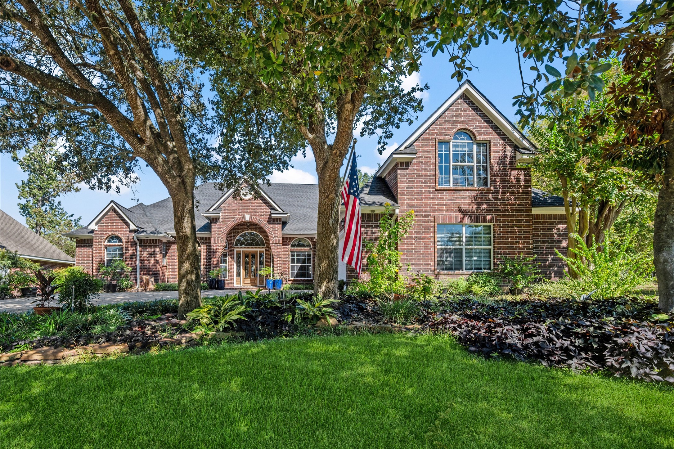 319 Palais Verde Road Montgomery, TX 77356 - Photo 2 of 40 This picturesque brick home features a well-maintained lawn with mature trees and a charming front entryway. The American flag adds a welcoming touch to the curb appeal.