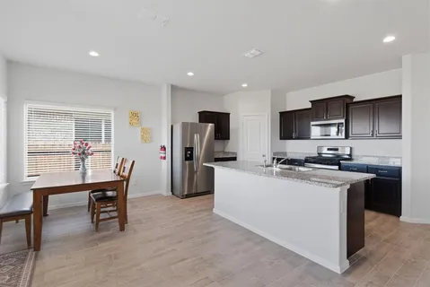 a kitchen with stainless steel appliances kitchen island granite countertop a refrigerator a stove a sink a dining table and chairs