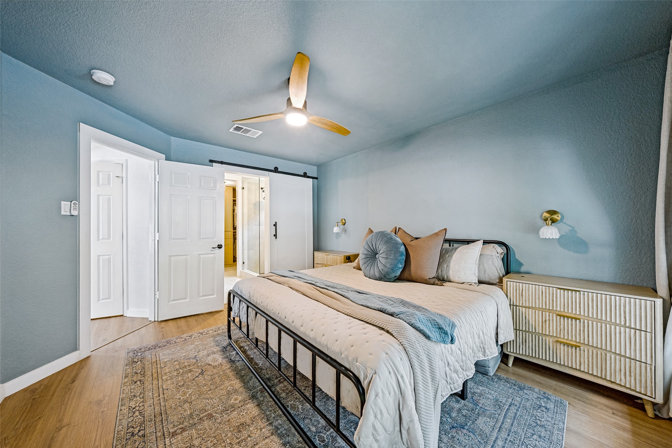 9205 Rowlands Sayle Road Austin, TX 78744 - Photo 16 of 25 The tranquil bedroom offers a quiet retreat with a classic ceiling fan, barn door, and sleek wood flooring.
